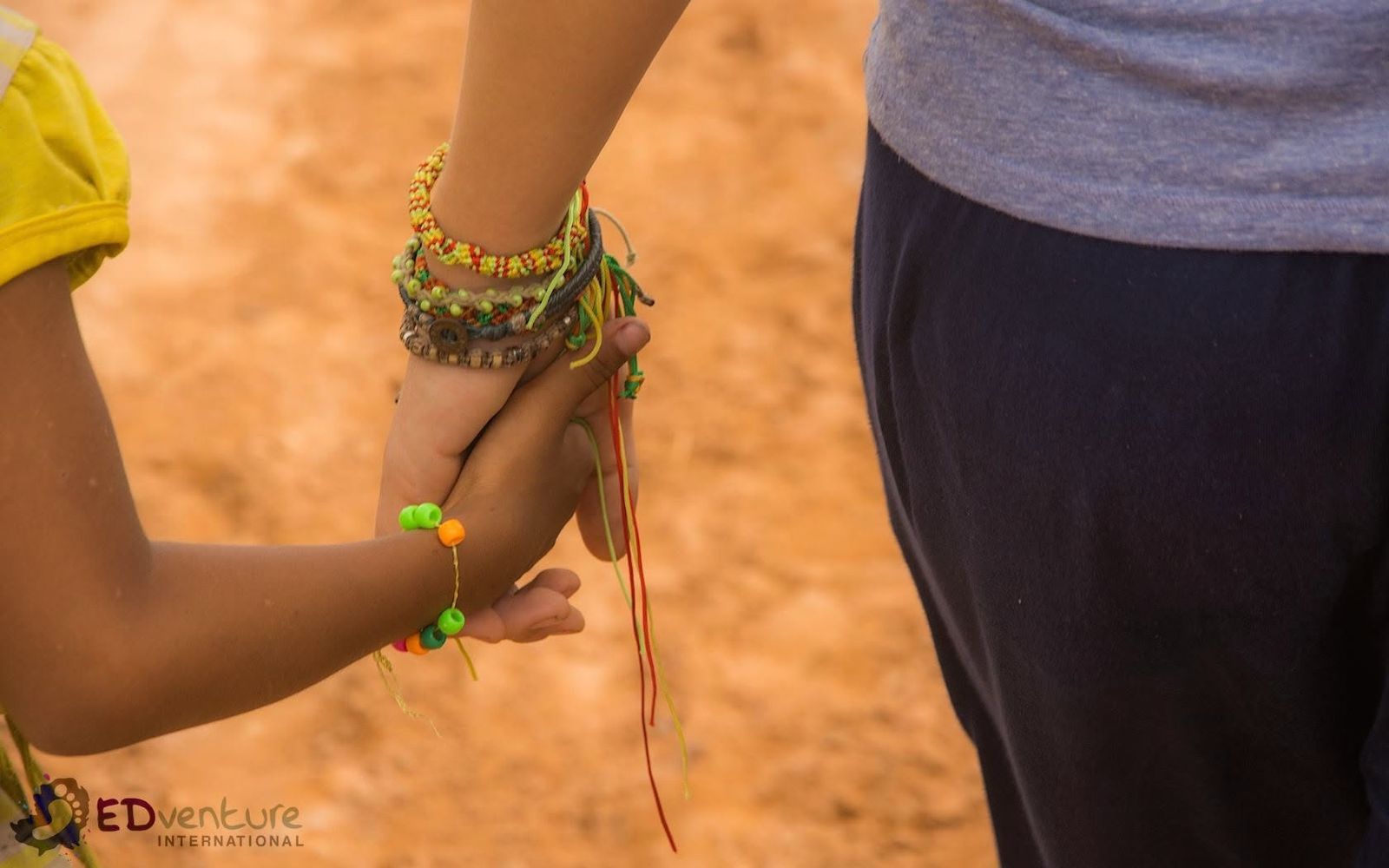 Walking alongside — EDGE Worldwide in Cambodia A Cambodian child and an EDGE Worldwide team member walking hand in hand along a dirt path