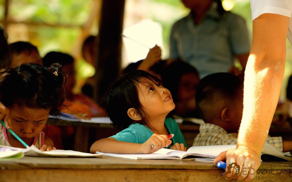 A young Cambodian student looking up to her teacher during a lesson supported by EDGE Worldwide