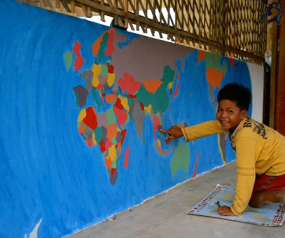 A Cambodian student pointing to Cambodia on a hand-painted world map mural at an EDGE Worldwide partner school