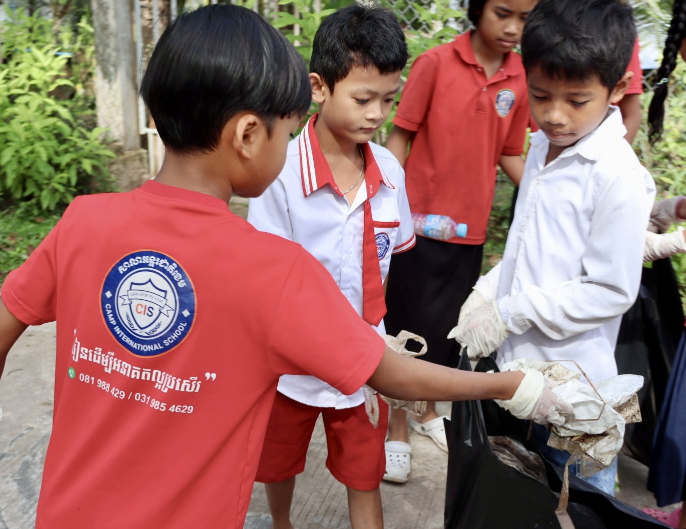Students in school uniforms collect rubbish into a bag during the Beong Touk community clean-up