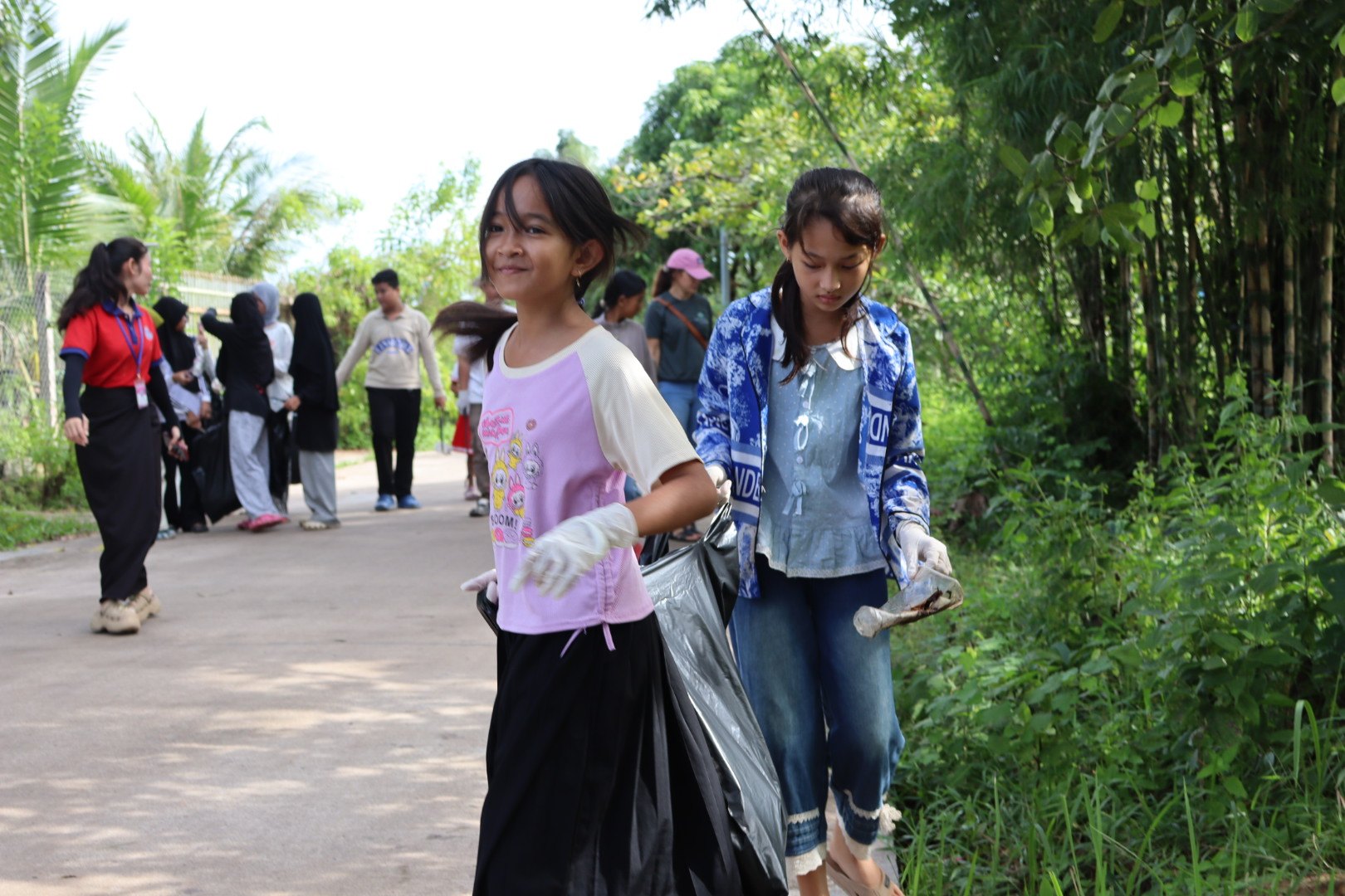 Students wearing gloves carry a rubbish bag along a village lane during the Beong Touk clean-up