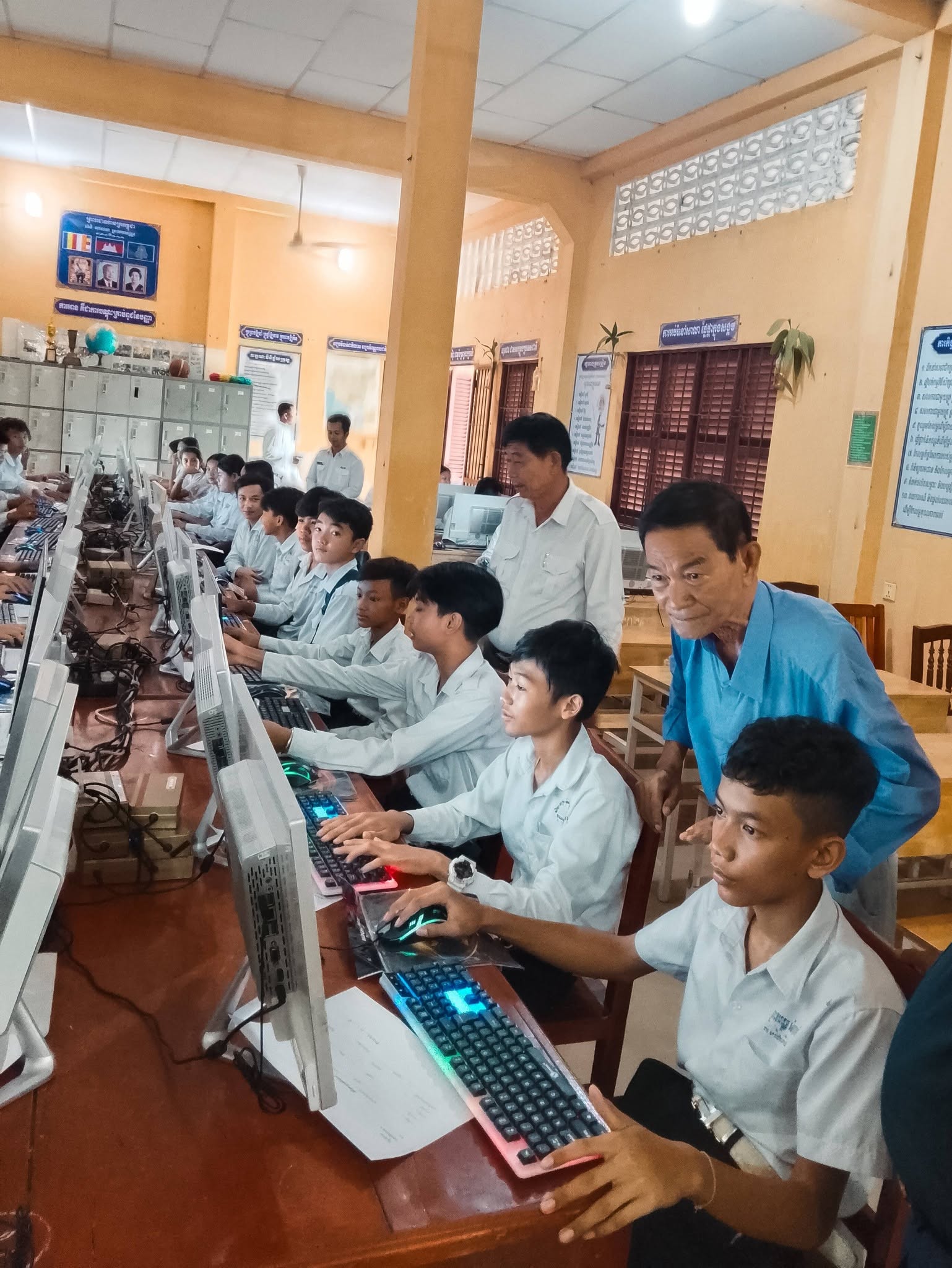 A teacher assisting students at computers in the IT lab