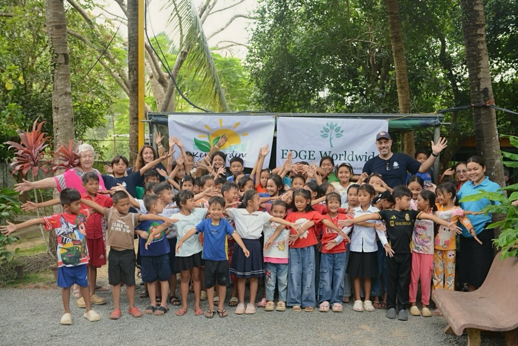 Children and adults gathered in front of Kep Gardens and EDGE Worldwide banners.