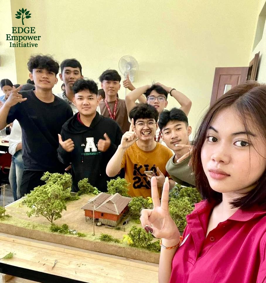 Students gathered around a model of a house surrounded by trees in a classroom