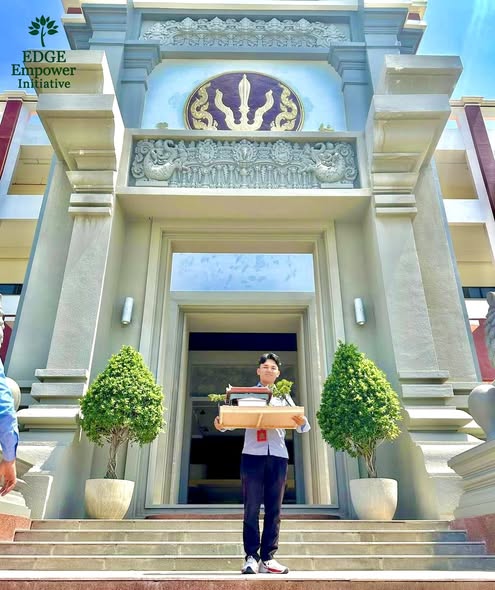 A student holding an architectural model on the steps of a building with decorative columns