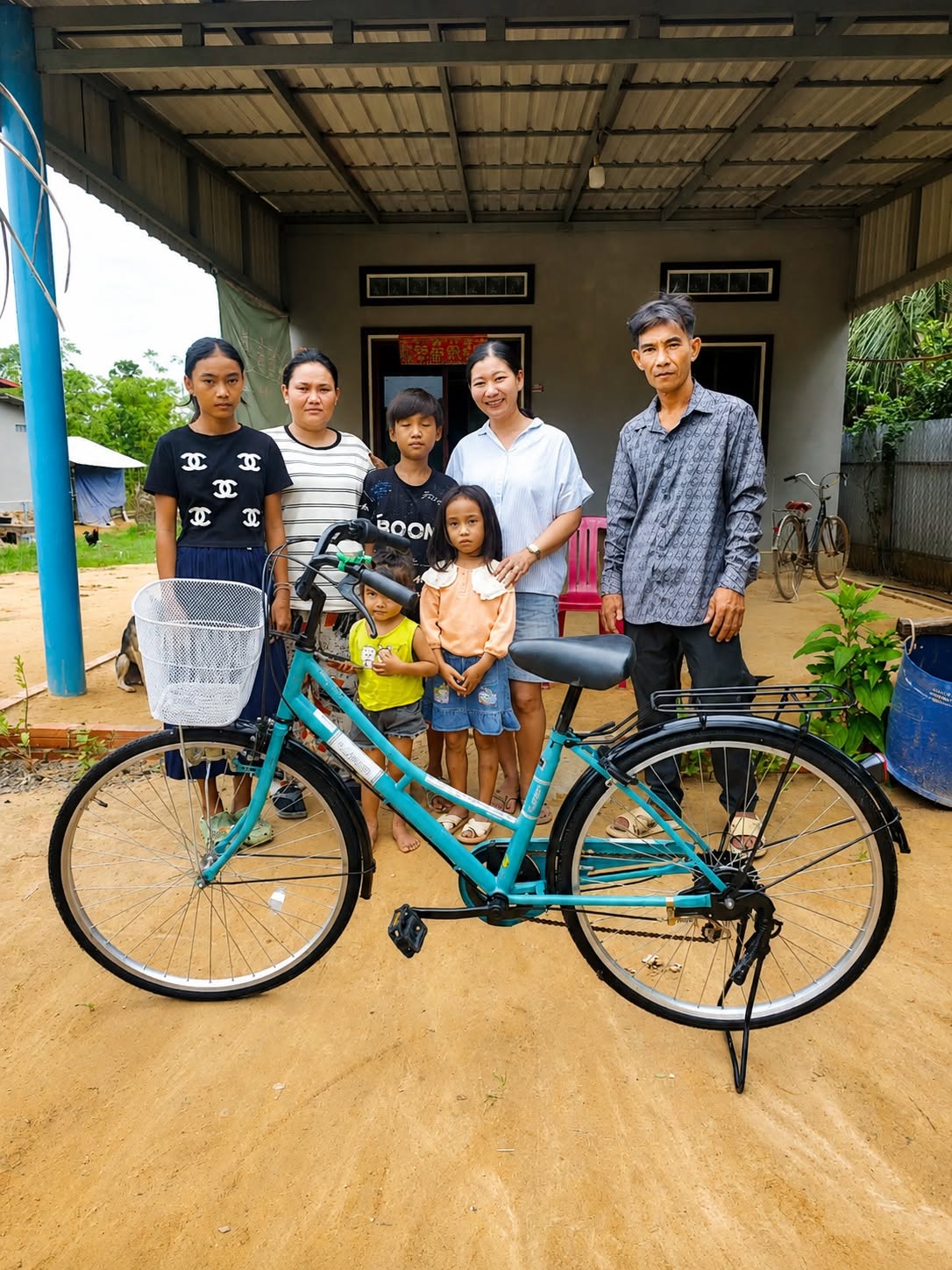 Adults and children gathered behind a blue bicycle outside a house.