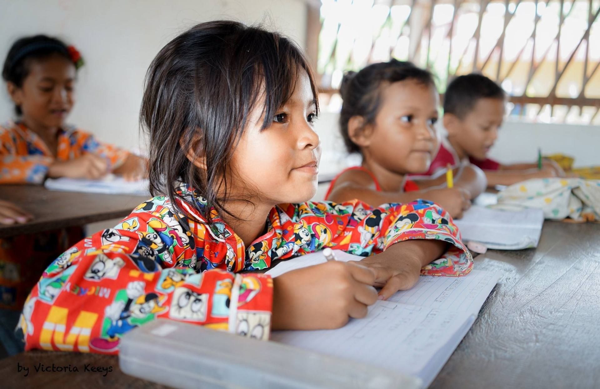 Cambodian schoolchildren writing in exercise books at a shared classroom desk